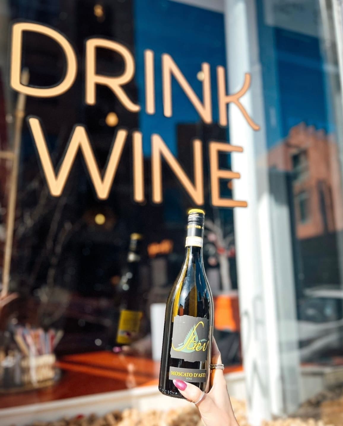 A bottle of Moscato held up against the Drink Wine window at Wax + Wine