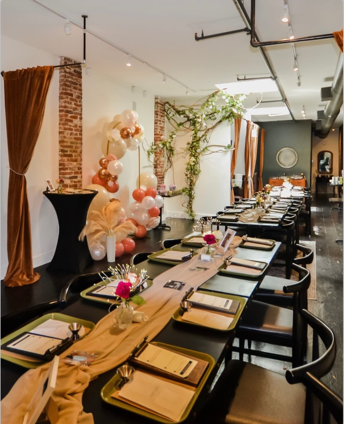A communal table set with a rose-gold balloon arch, ivy, and place settings, ready for an event