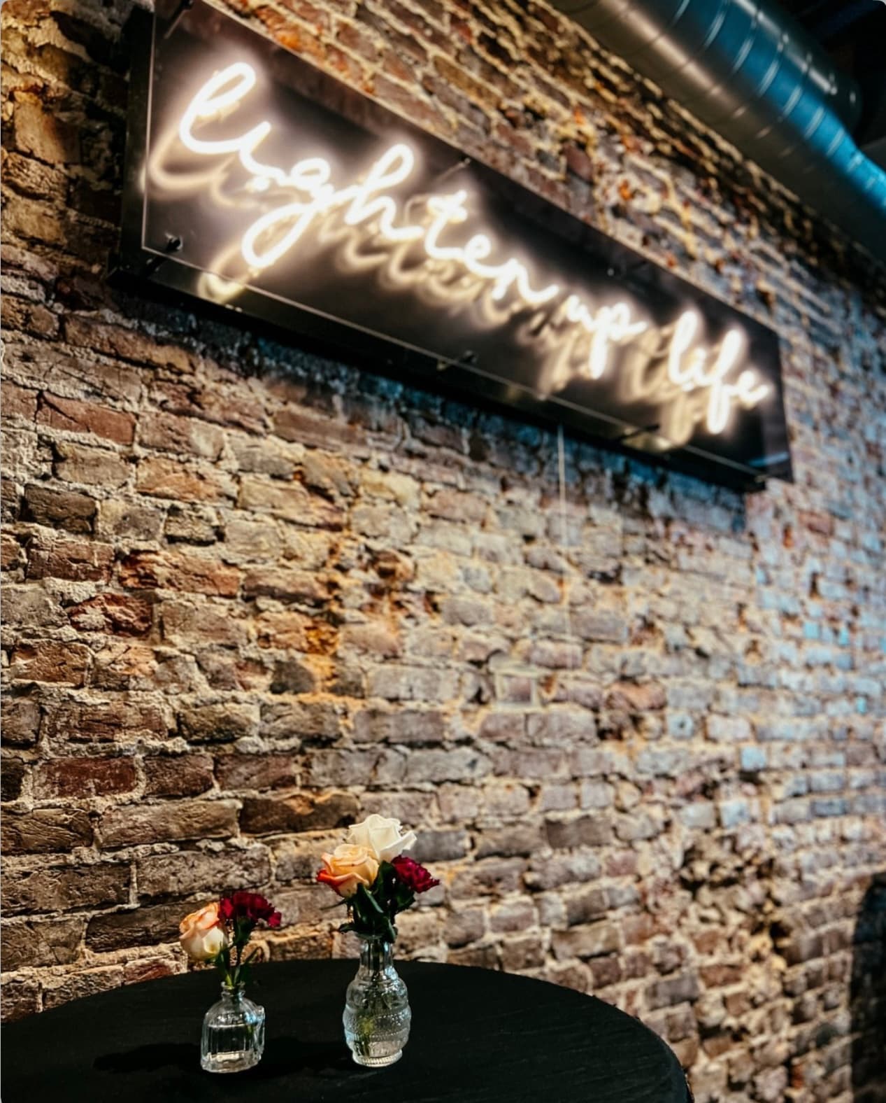 The lighten-up-life neon sign at Wax + Wine, set above a bistro table with roses