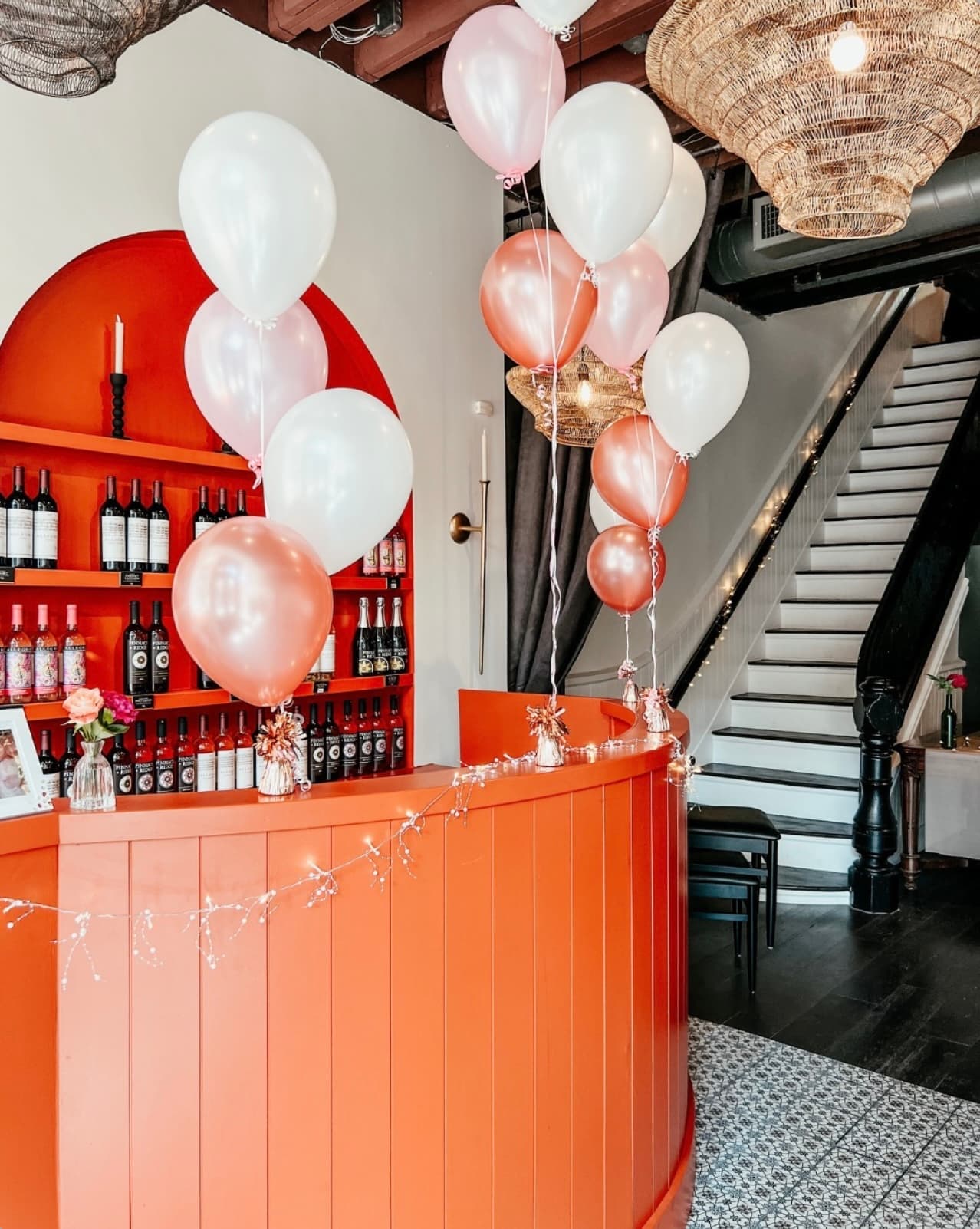The terra-cotta wine bar at Wax + Wine dressed with rose-gold balloons, with a staircase visible behind