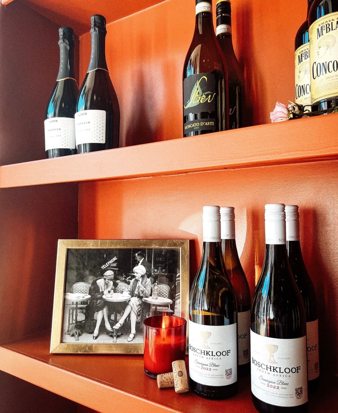 The wine shelf at Wax + Wine, set against a warm terracotta wall