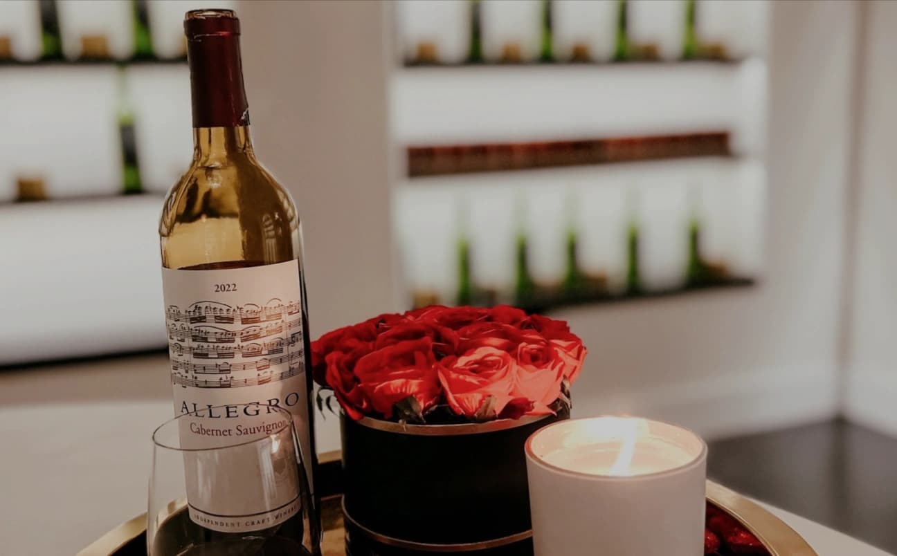 A bottle of wine, roses, and a lit candle on a tray at Wax + Wine